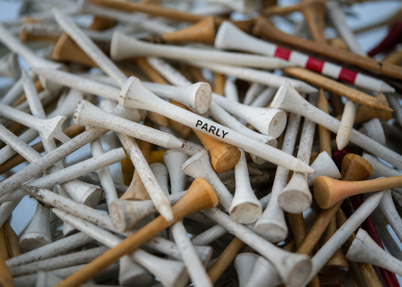 A pile of wooden tees with a single PARLY-branded tee on top