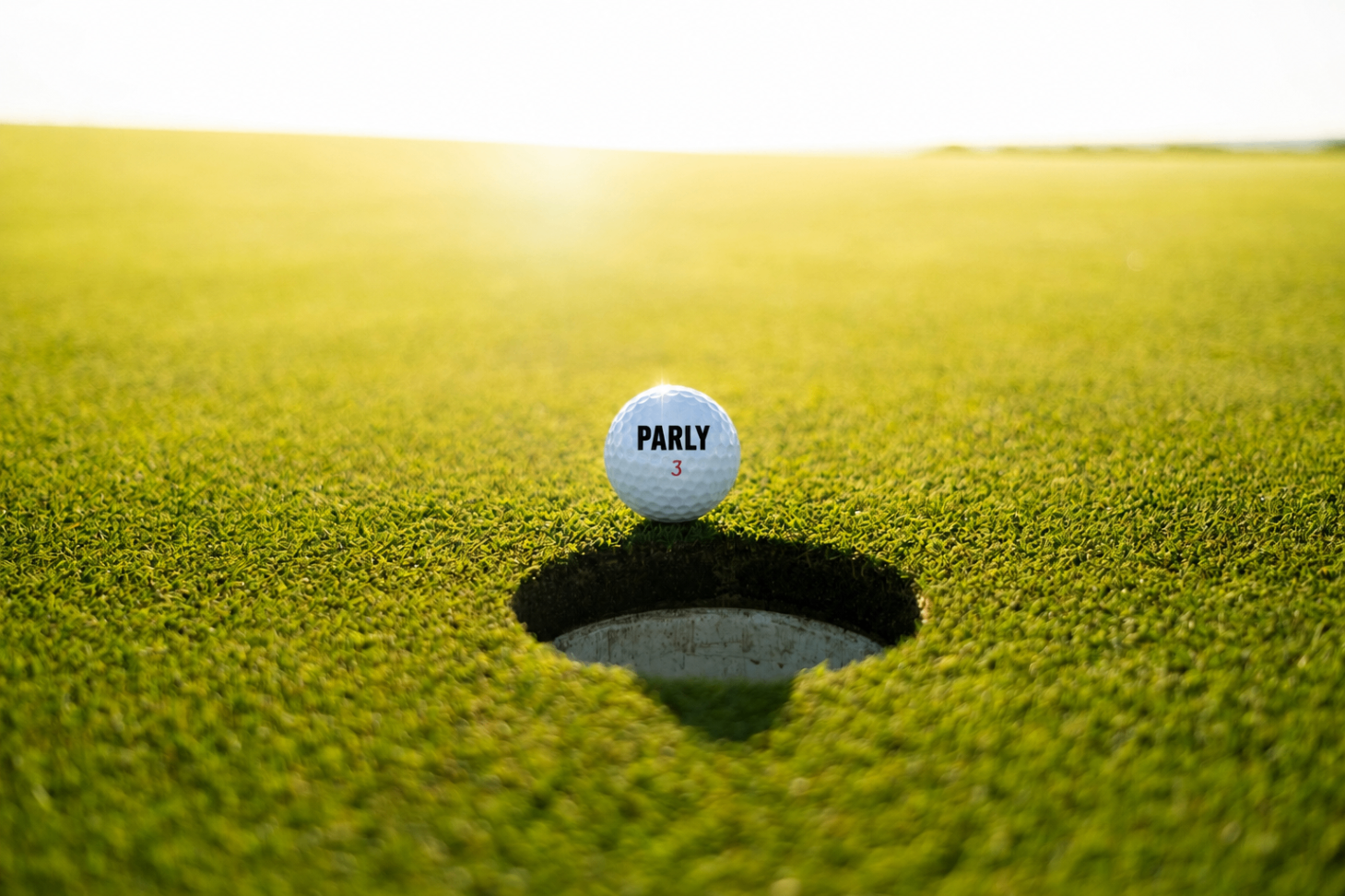 A PARLY golf ball resting on the lip of the hole at sunset