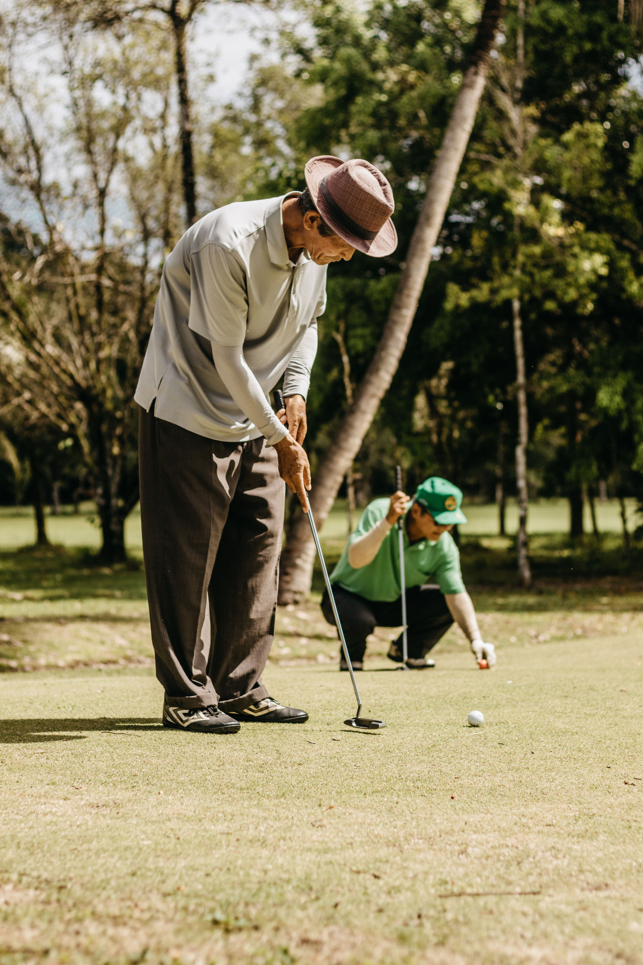 Two golfers reading a putt on a tree-lined green